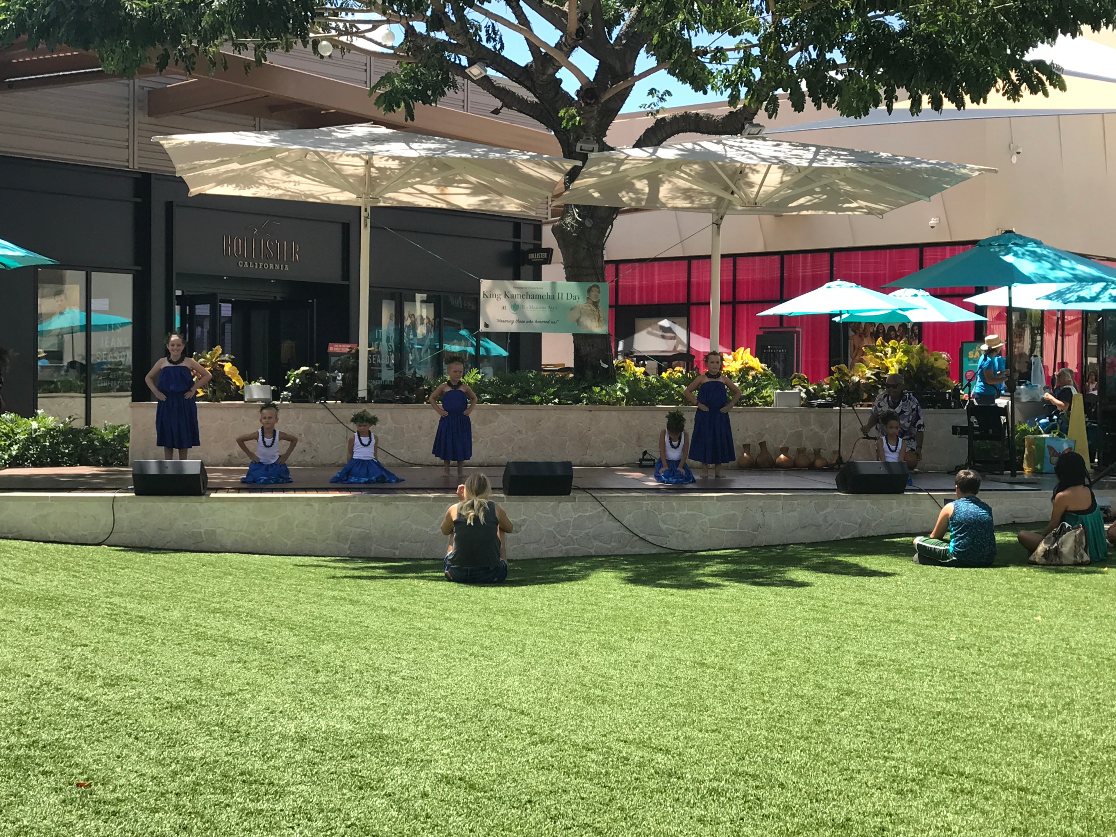 Hula dancers in blue performing on outdoor stage