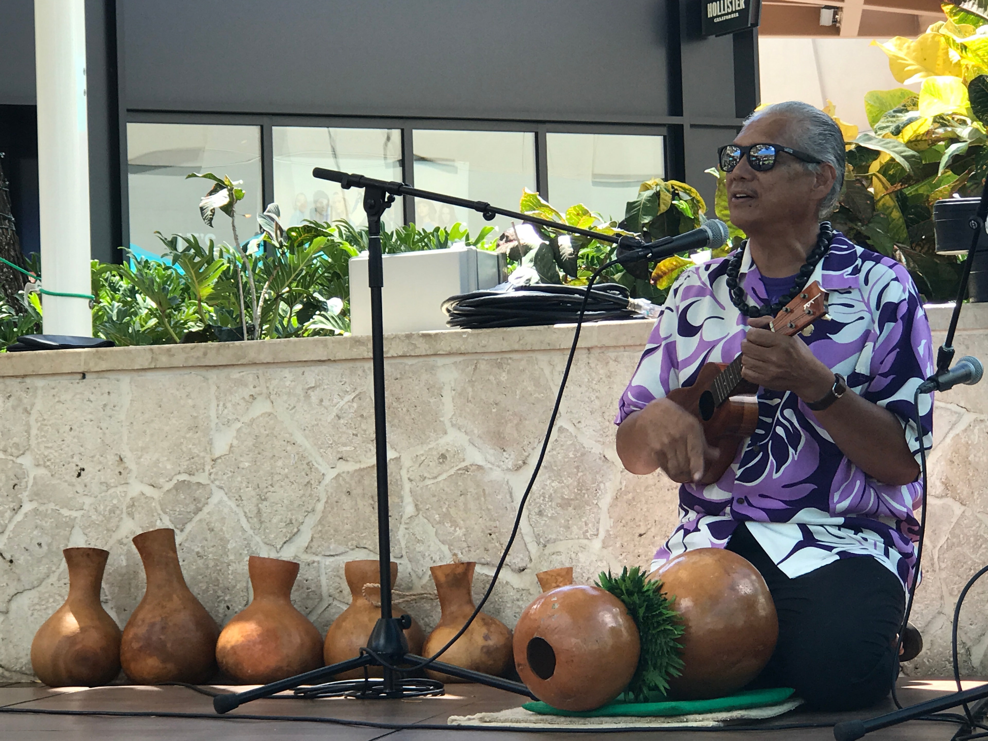Musician performing ukulele with traditional ipu gourds at outdoor event