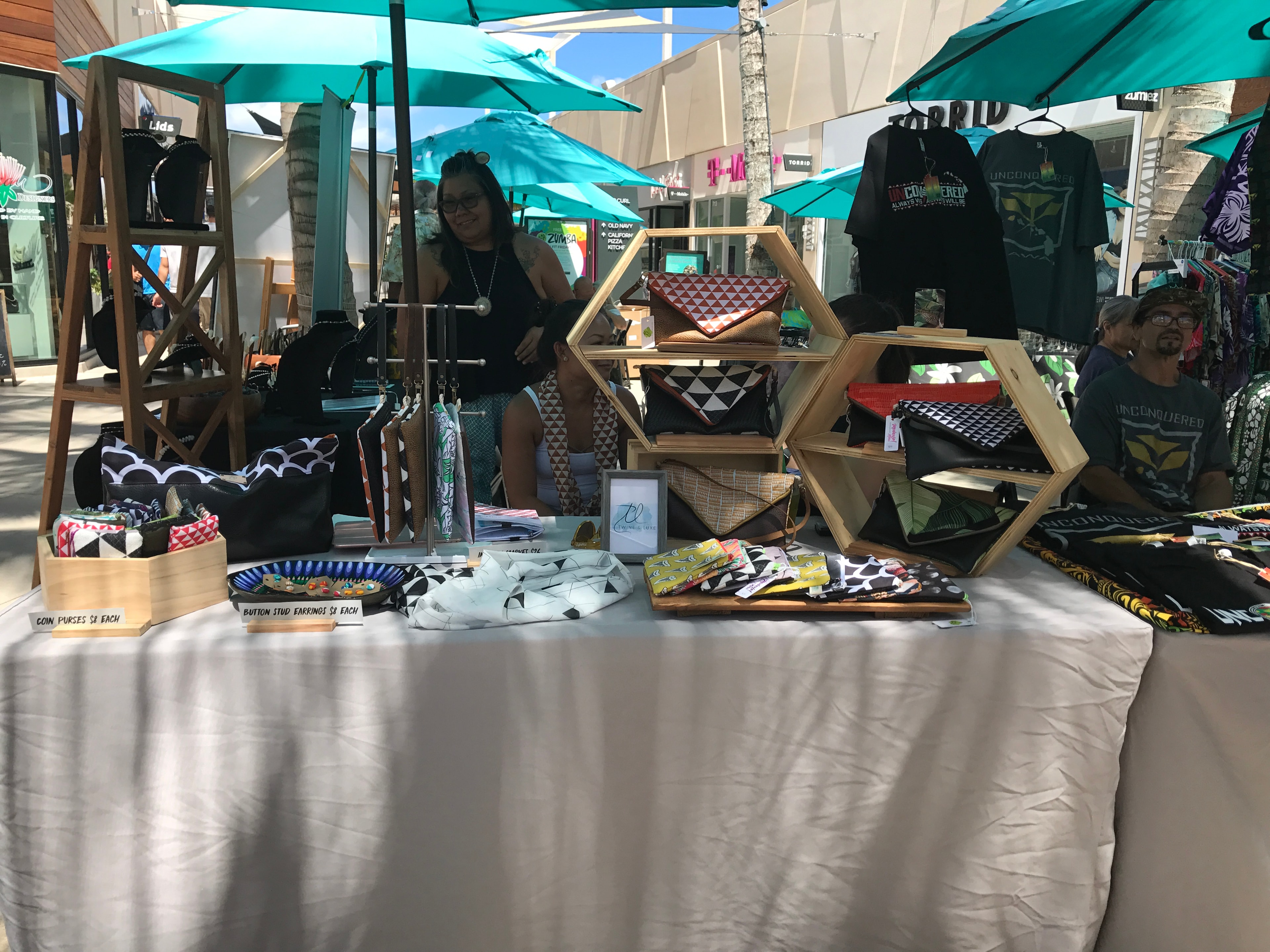 Vendor booth displaying geometric patterned clutch purses and accessories with hexagonal wood shelving