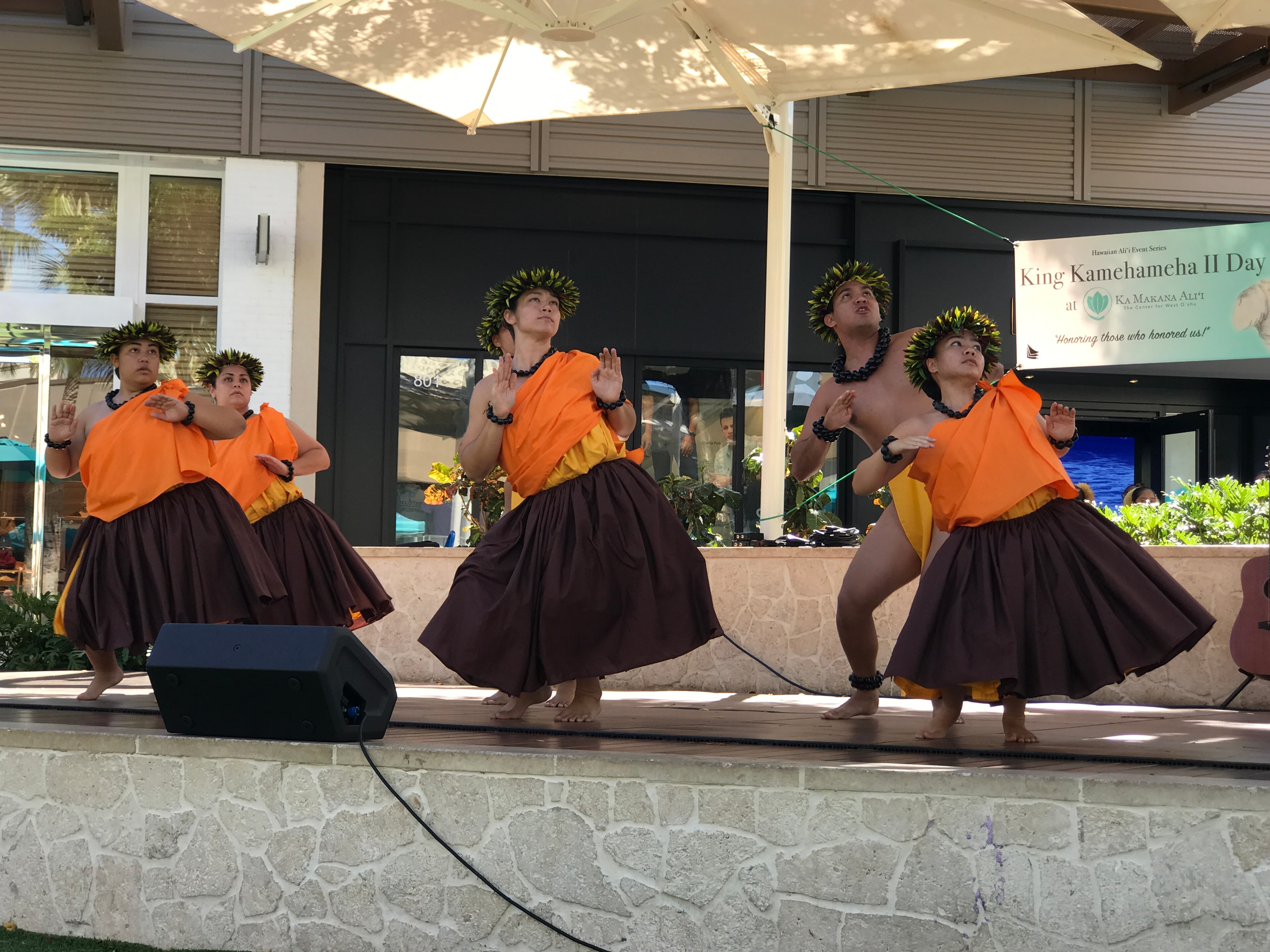 Hula halau in orange and brown performing in unison at King Kamehameha II Day outdoor stage