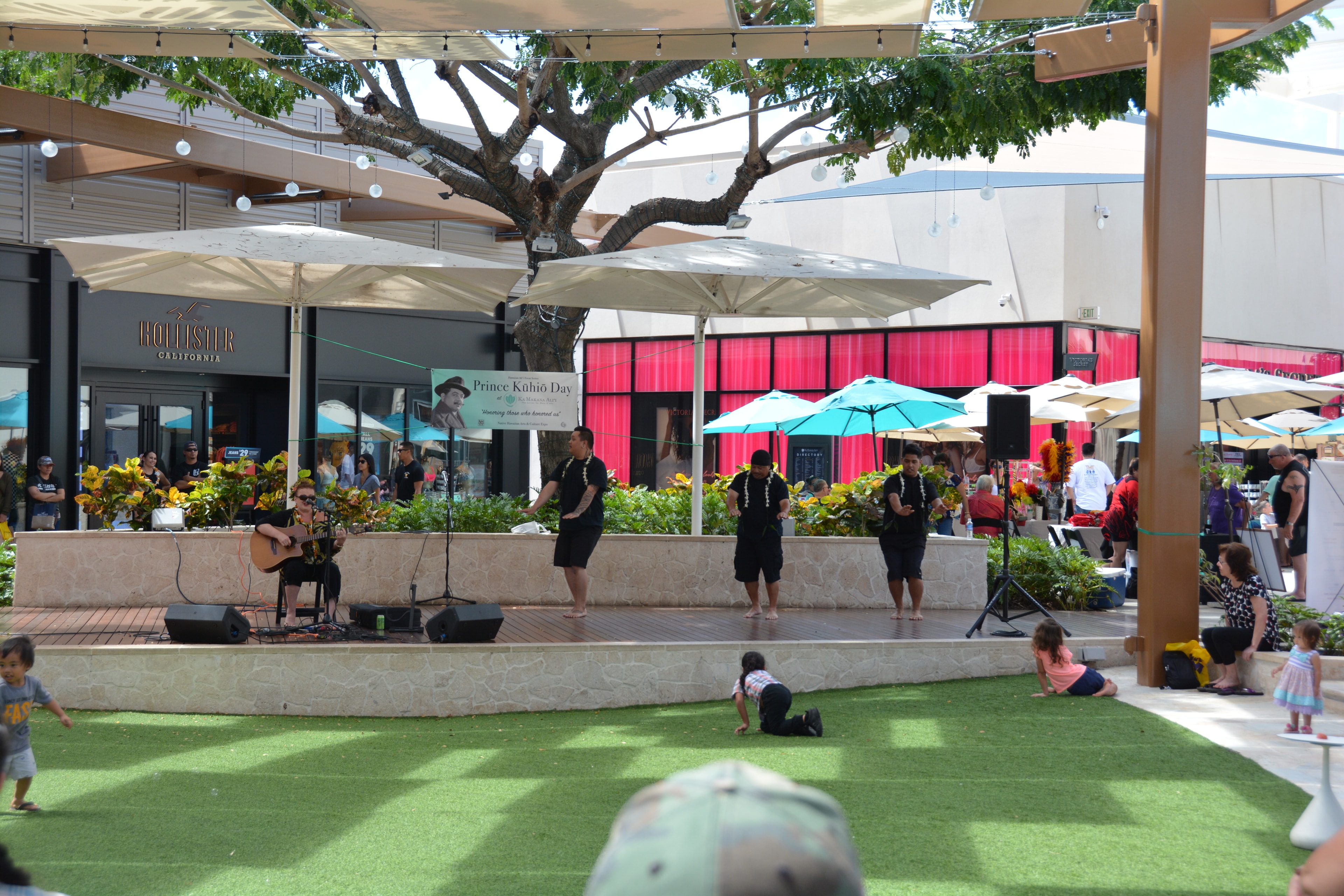 Hawaiian male dancers with lei performing at Prince Kūhiō Day stage at Ka Makana Aliʻi