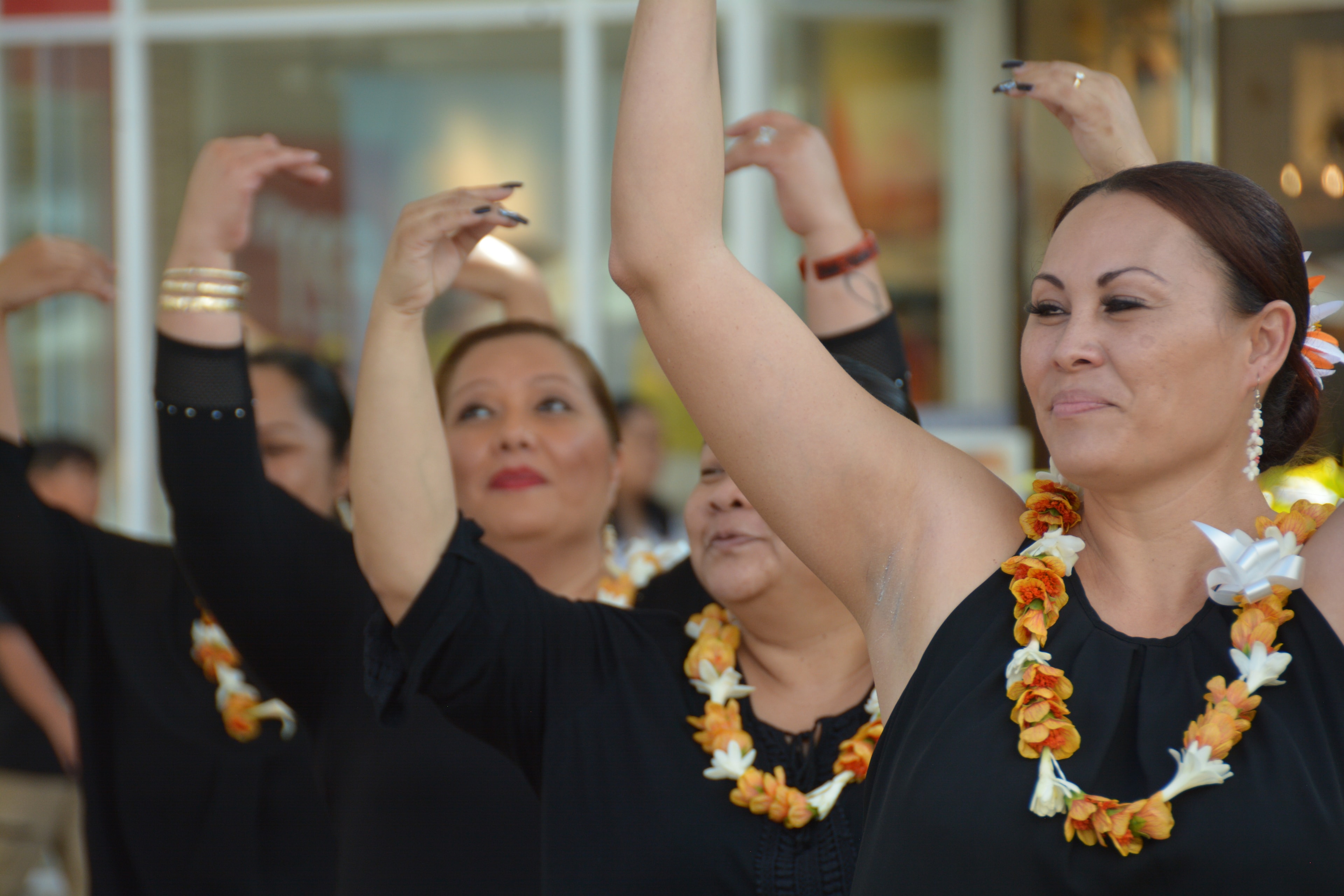 Close-up of Hawaiian hula dancers with orange lei performing arms raised