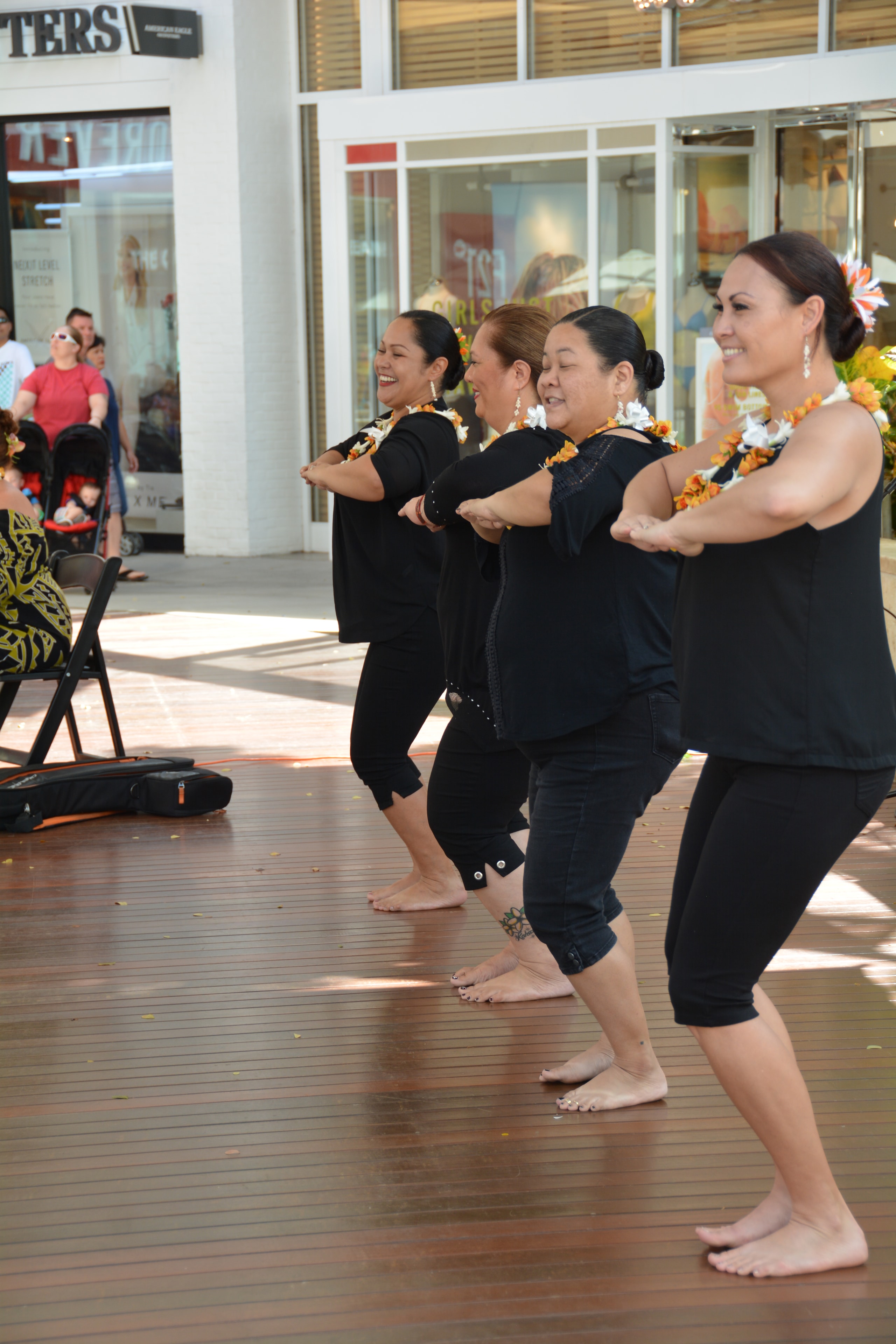 Hawaiian women dancers smiling and performing hula at outdoor mall stage