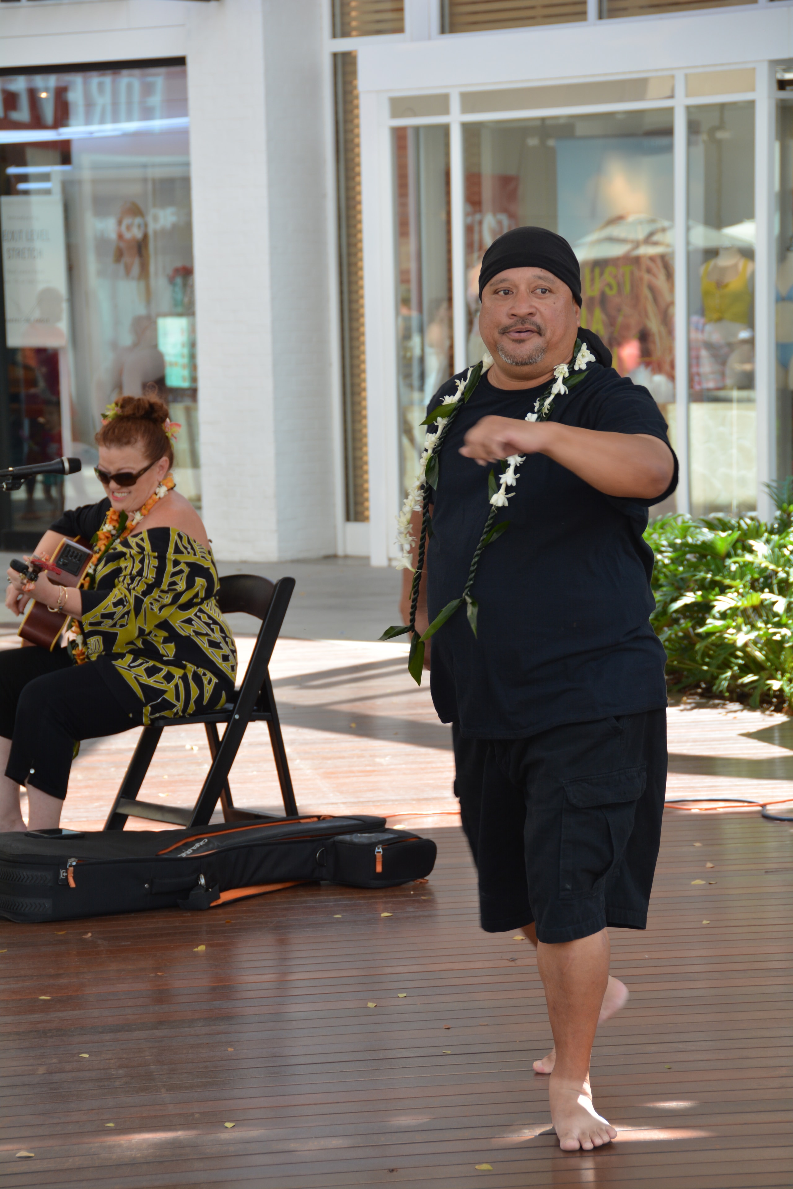 Hawaiian male dancer with white lei performing hula with ukulele accompaniment at outdoor stage