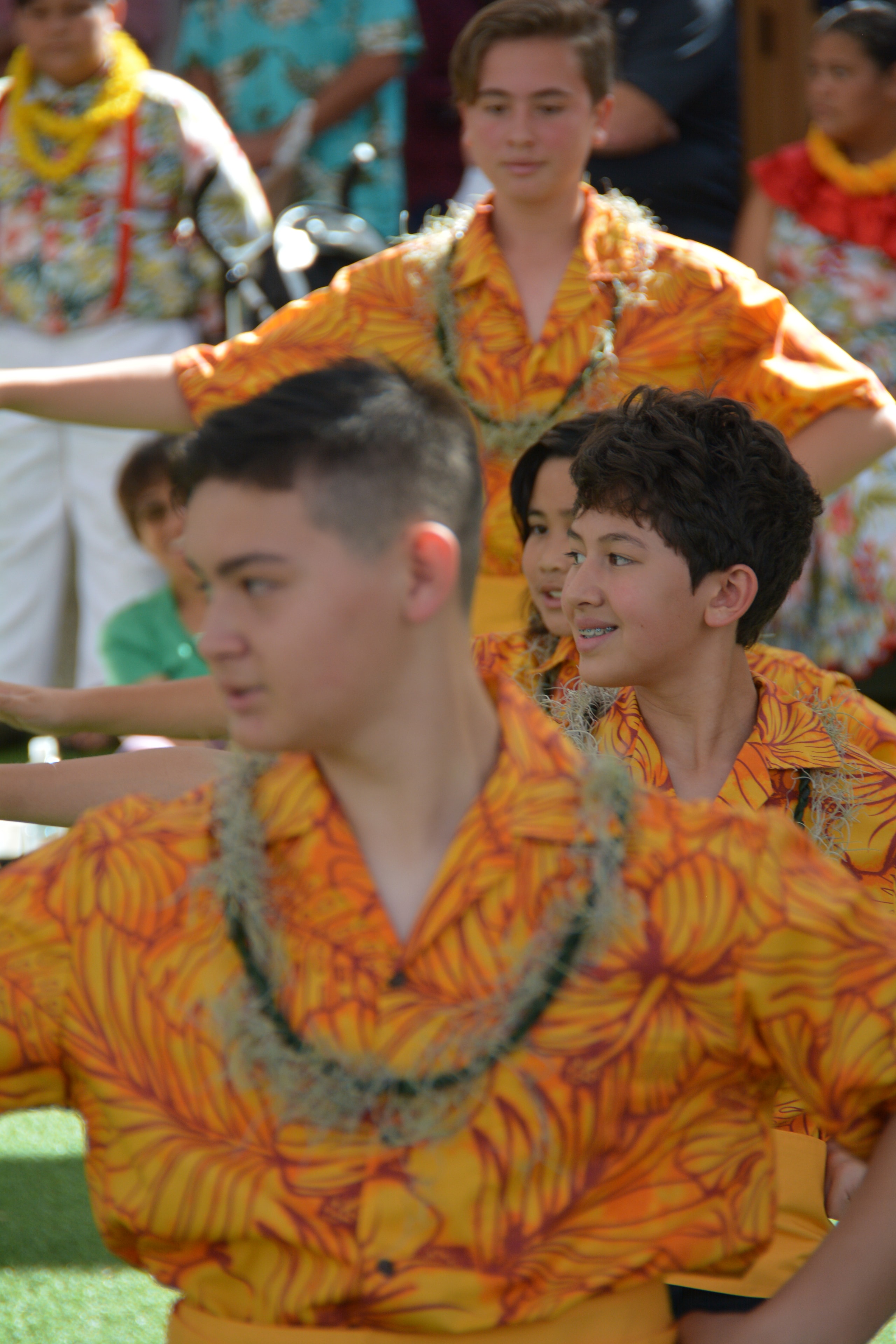 Close-up of young male hula dancers in orange floral shirts performing seated hula
