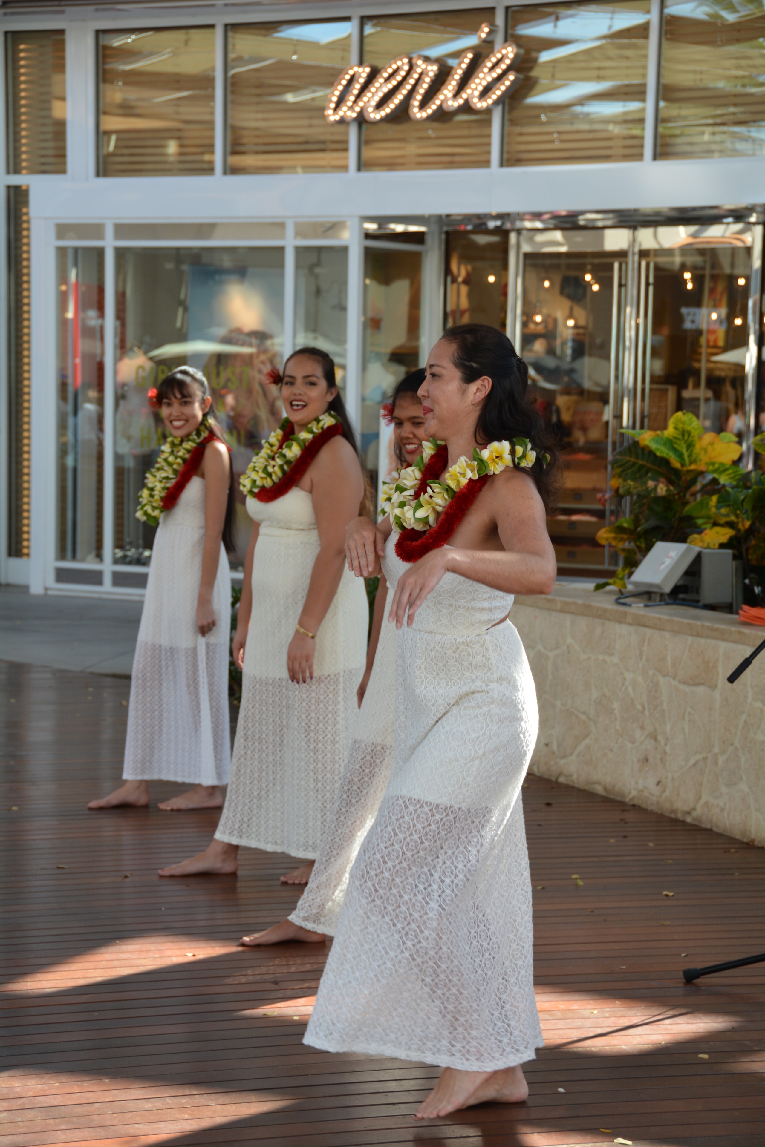 Four women in white lace dresses with red and yellow lei performing hula at Ka Makana Aliʻi