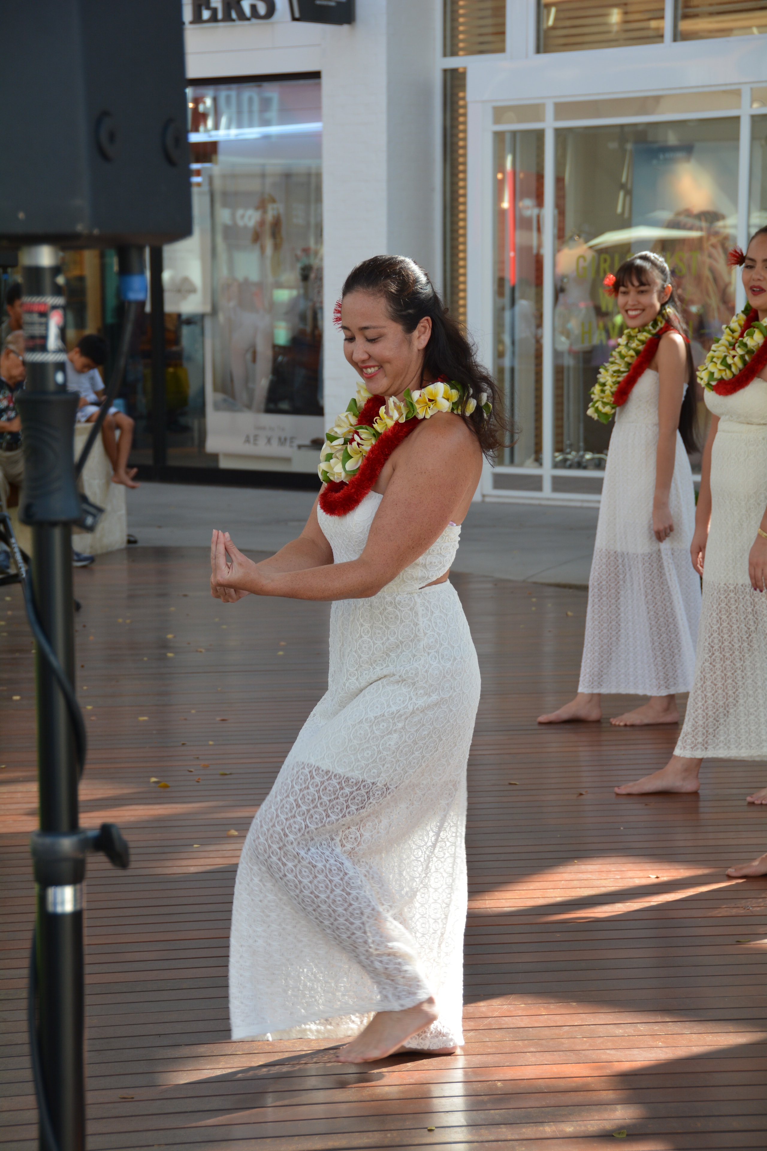 Hawaiian women in white lace dresses with plumeria lei performing hula at outdoor shopping center stage