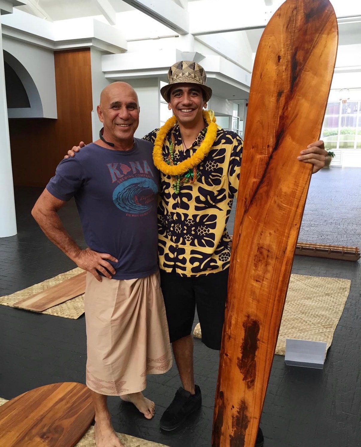 Two men posing with wooden surfboard indoors