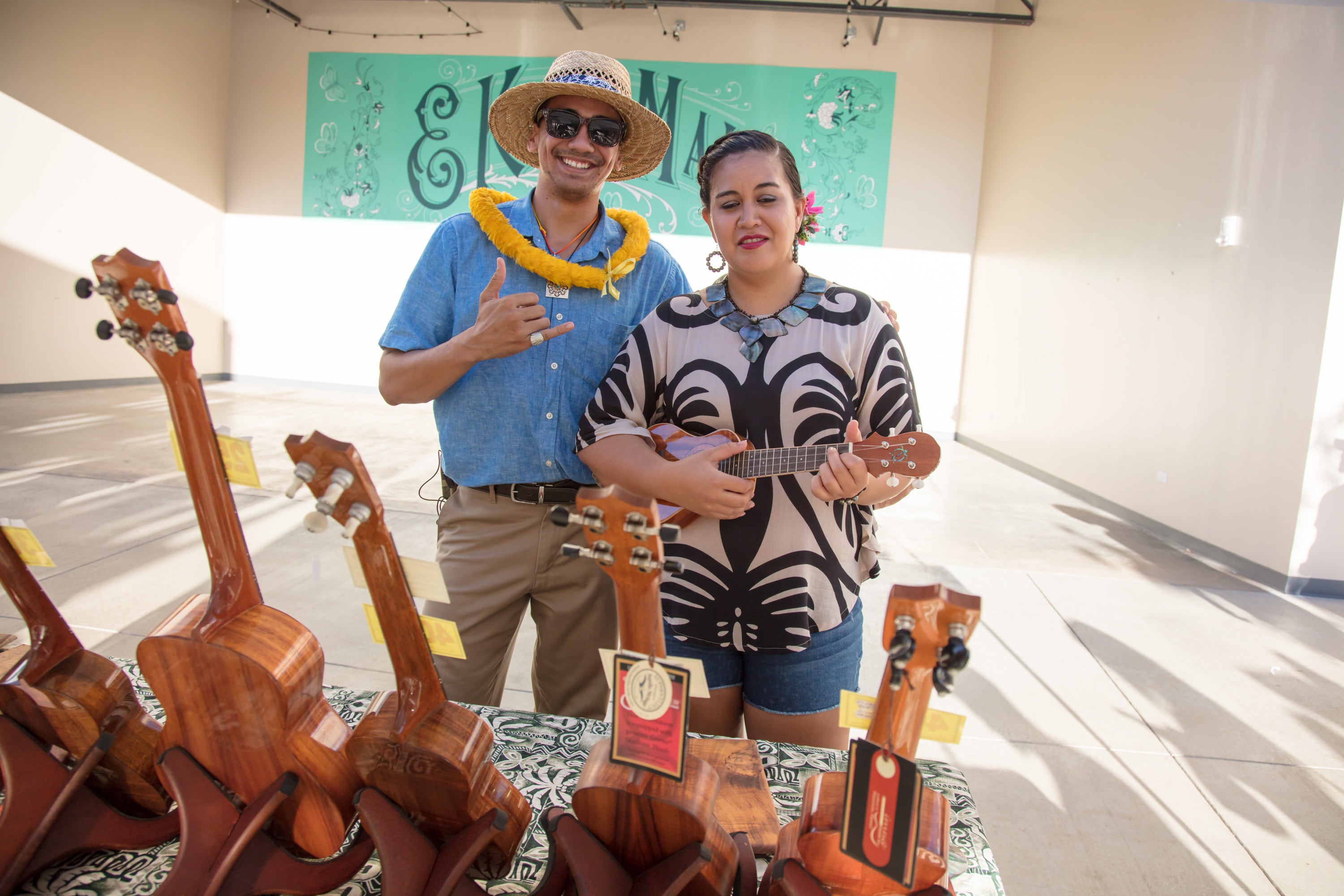 Two musicians displaying handcrafted ukuleles indoors